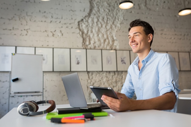 Hipster attractive man using devices, working on laptop and tablet computer