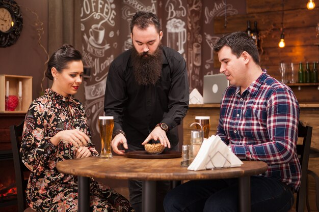 Hipster barman giving the order to beautiful young couple.Great Pub.