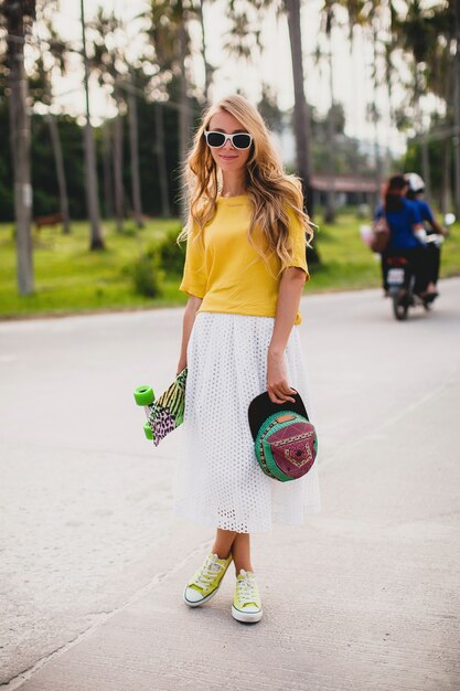 Hipster cool woman with skate board and cap posing smiling on vacation