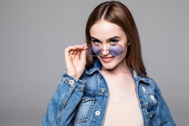 Hipster girl wearing blank gray t-shirt, jeans and backpack posing against gray wall