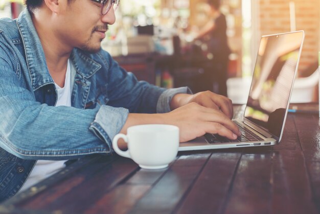 カフェでタブレットコンピュータを使用しながら、ヒップスターの男性がコーヒーを飲みます。