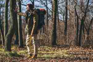 Foto gratuita uomo di hipster che viaggia con lo zaino nella foresta di autunno che indossa giacca calda, cappello, turista attivo, esplorando la natura nella stagione fredda