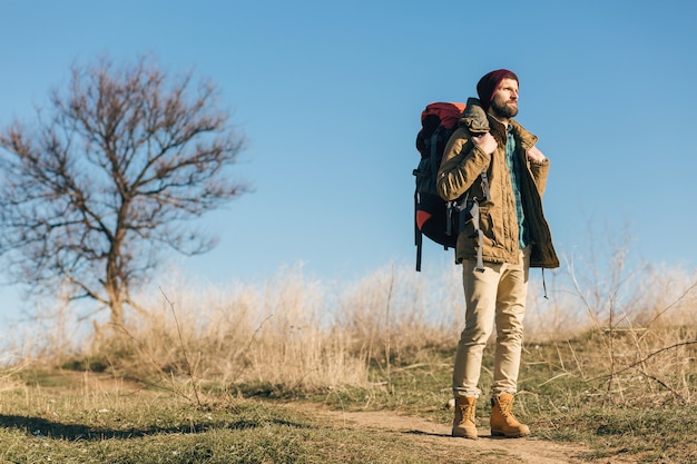 Hipster man traveling with backpack in autumn forest wearing warm jacket, hat, active tourist, exploring nature in cold season