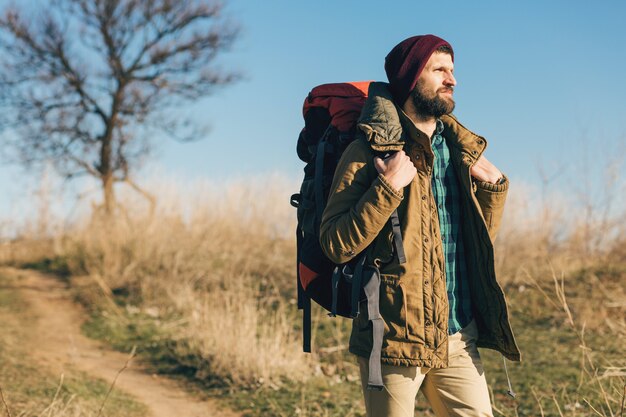 Hipster man traveling with backpack in autumn forest wearing warm jacket, hat, active tourist, exploring nature in cold season