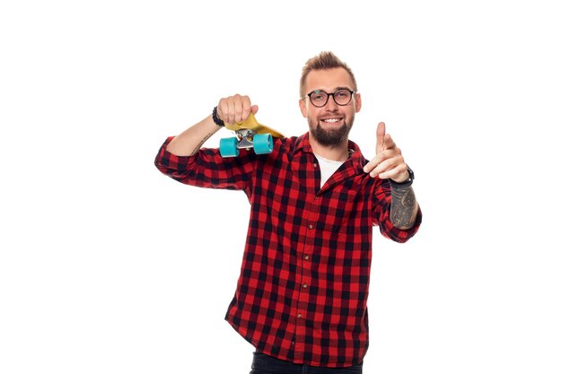 Hipster man over white background holding yellow skateboard. Carefree youth and freedom. Active guy in plaid shirt with copy space