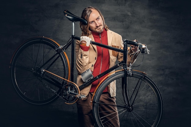 L'uomo hipster con lunghi capelli biondi tiene una bicicletta a velocità singola sulla spalla.