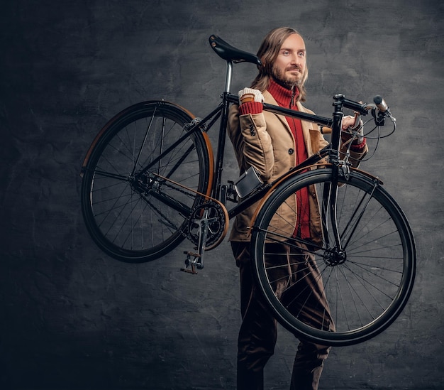 Hipster man with long blond hair holds single speed bycycle on his shoulder.