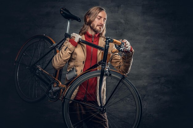 Hipster man with long blond hair holds single speed bycycle on his shoulder.