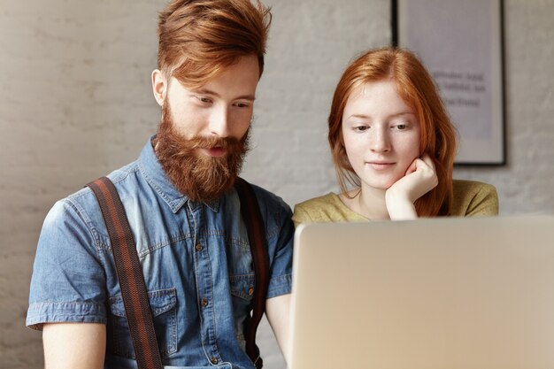 Studente di hipster con peli sul viso utilizzando laptop con giovane donna rossa.