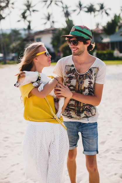 熱帯のビーチ、白い砂浜、クールな服装、ロマンチックな気分、楽しい、日当たりの良い、男性女性、休暇で遊んで犬の子犬ジャックラッセルを歩いて恋に流行に敏感な若いスタイリッシュな流行に敏感なカップル