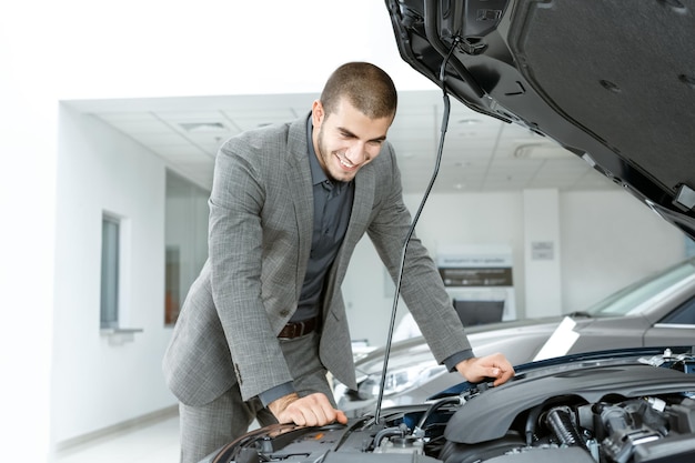 Foto gratuita il suo nuovo amore bel ragazzo in giacca e cravatta che controlla un'auto prima di acquistarla