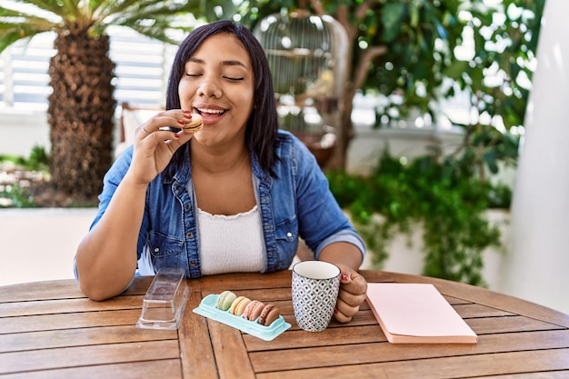 Free photo hispanic brunette woman drinking a coffee and eating pastries at the terrace