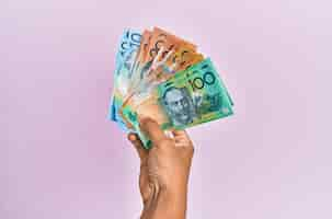 Free photo hispanic hand holding australian dollars banknotes over isolated pink background.