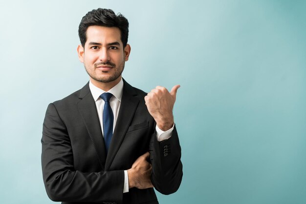 Hispanic male executive gesturing at copy space while making eye contact in studio