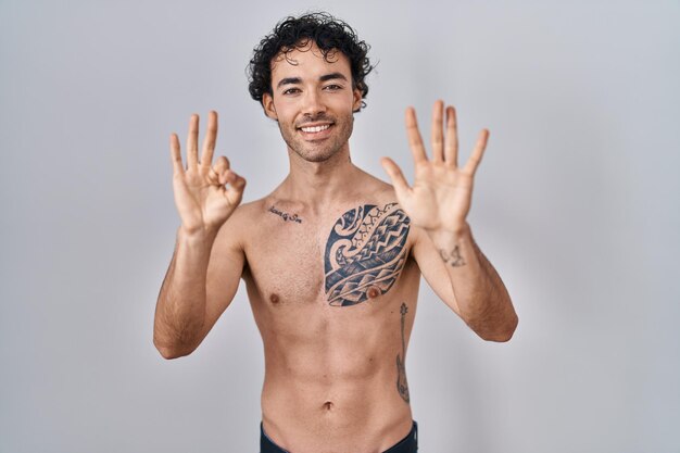 Hispanic man standing shirtless showing and pointing up with fingers number eight while smiling confident and happy