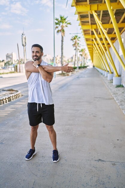 Hispanic man stretching arm after working out outdoors on a sunny day