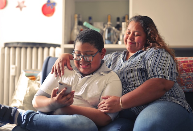 Hispanic mother and her son working with a smartphone sitting on the couch