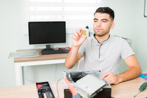 Tecnico ispanico che esamina un chip del microprocessore. uomo del computer che controlla l'hardware della cpu di un cliente presso l'officina di riparazione