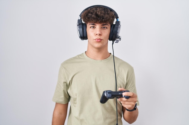 Free photo hispanic teenager playing video game holding controller looking at the camera blowing a kiss on air being lovely and sexy. love expression.