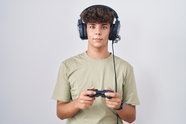 Free photo hispanic teenager playing video game holding controller relaxed with serious expression on face. simple and natural looking at the camera.