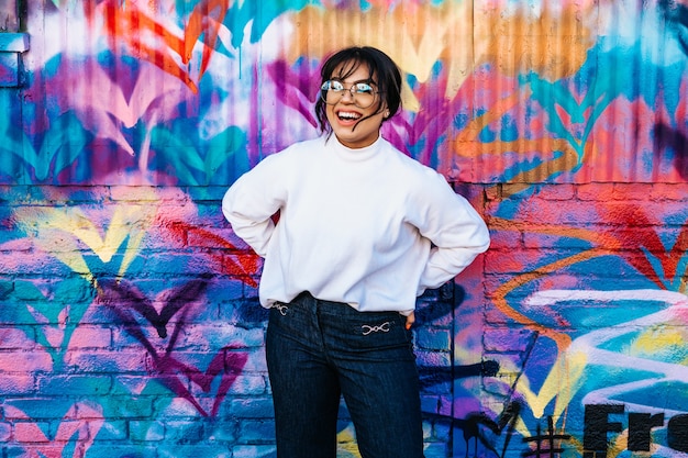 A Hispanic woman cheerfully laughing with a flowered graffiti wall