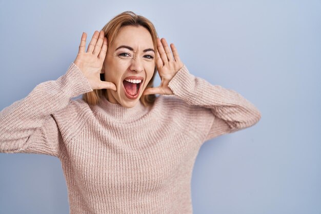 Hispanic woman standing over blue background smiling cheerful playing peek a boo with hands showing face. surprised and exited