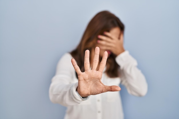 Hispanic woman standing over isolated background covering eyes with hands and doing stop gesture with sad and fear expression. embarrassed and negative concept.