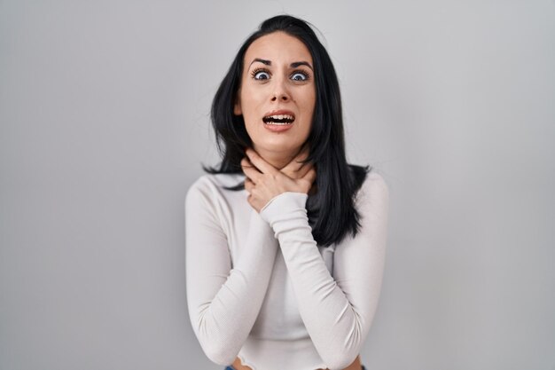 Hispanic woman standing over isolated background shouting and suffocate because painful strangle health problem asphyxiate and suicide concept