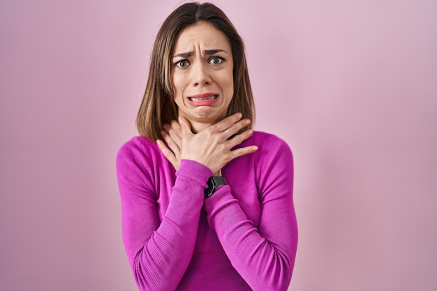 Hispanic woman standing over pink background shouting suffocate because painful strangle health problem asphyxiate and suicide concept