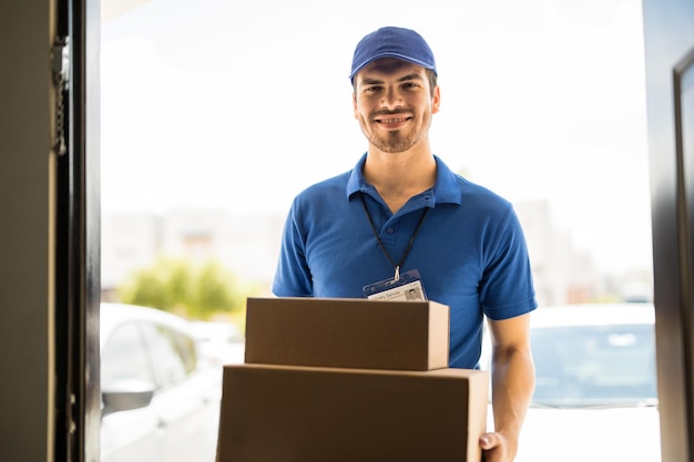 Hispanic young delivery man bringing some packages to a house and smiling