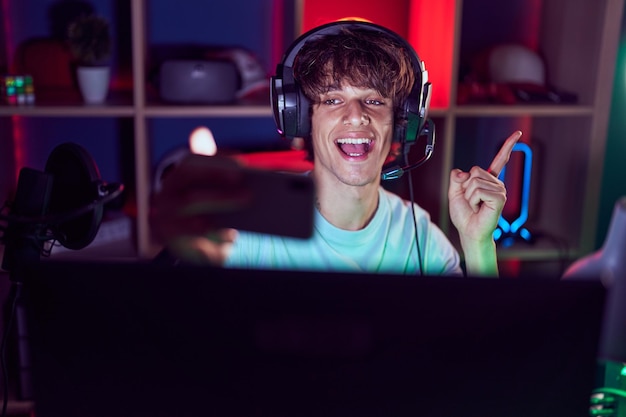 Foto gratuita giovane ispanico che gioca ai videogiochi con lo smartphone che sorride felice puntando con la mano e il dito di lato