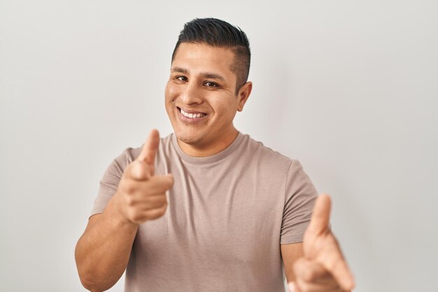 Hispanic young man standing over white background pointing fingers to camera with happy and funny face good energy and vibes