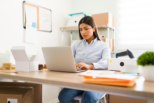 히스패닉계 젊은 여성이 사무실 책상에 앉아 노트북으로 작업합니다. 스타트업 사업에서 성공하기 위해 노력하는 젊은 기업가