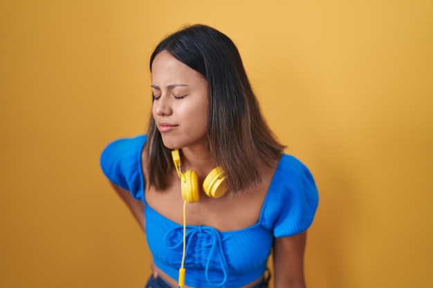 Free photo hispanic young woman standing over yellow background suffering of backache, touching back with hand, muscular pain