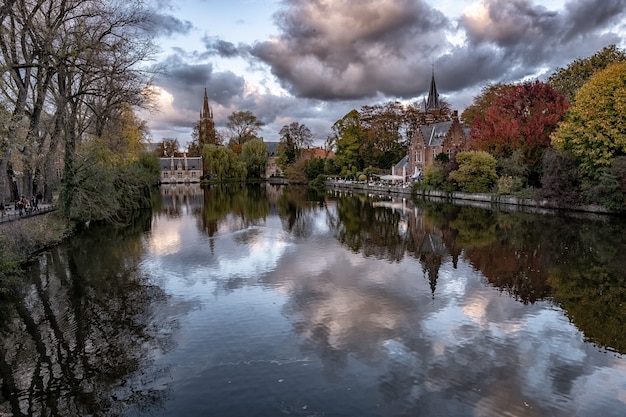 Historical castle surrounded by colorful trees reflected in the lake under the storm clouds