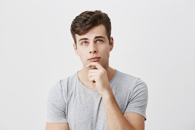 Hmm not bad. Concentrated thoughtful male student evaluating his chances to pass exam, keeps hand on chin, tries to decide what he deserves. People, lifestyle, face expressions.