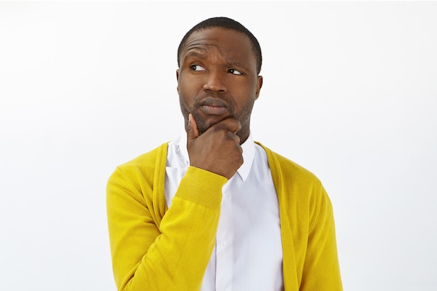 Hmm. Let me think. Stylish young mixed race man posing in studio, rubbing chin, raising eyebrow and looking sideways with doubtful uncertain facial expression, hesitating to make important decision