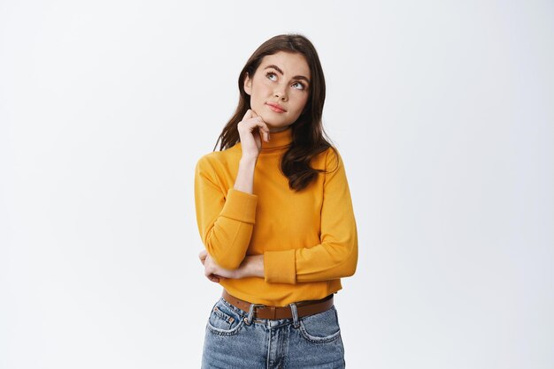 Hmm let me think Thoughtful young woman planning something looking at upper left corner and pondering imaging things on empty space white background