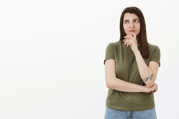 Free photo hmm need think about it. portrait of thoughtful focused smart and creative female coworker with tattoo doing brainstorm making up idea looking at upper left corner as remembering data over gray wall