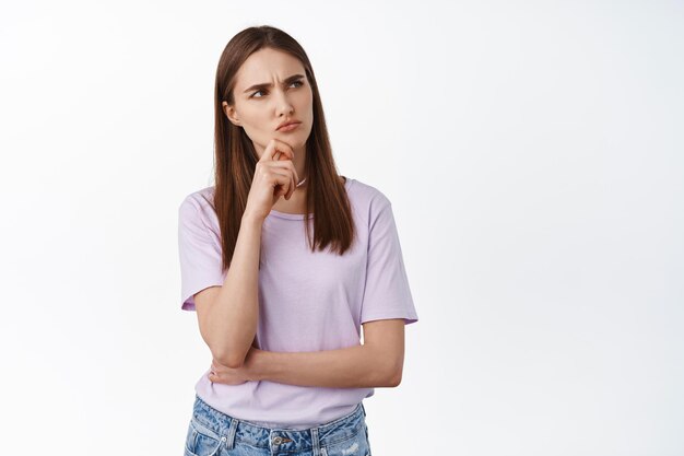 Hmm. Thoughtful girl looks at upper right corner suspicious, having doubts, thinking and makes decision, being unsure about something strange, white background