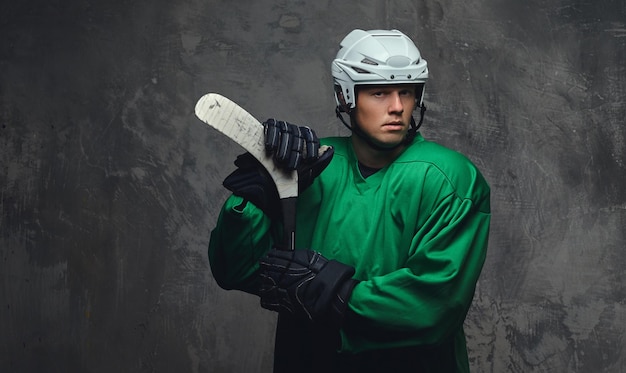 Giocatore di hockey che indossa indumenti protettivi verdi e casco bianco in piedi con la mazza da hockey. isolato su sfondo grigio.