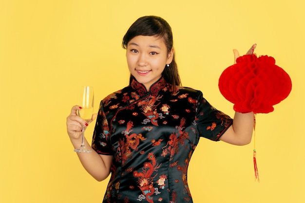 샴페인과 랜턴을 들고. 행복 한 중국 새 해 2020. 노란색 배경에 아시아 젊은 여자의 초상화. 전통 옷을 입은 여성 모델이 행복해 보입니다. 축하, 감정. Copyspace.