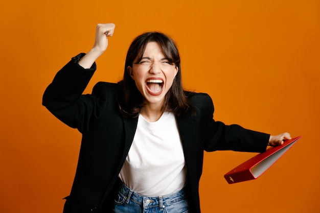 Holding folder with pen young beautiful female wearing black jacket isolated on orange background