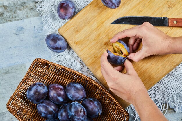 Holding fresh plum on wooden board with basket of plums.