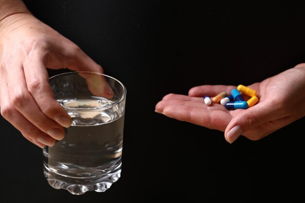 Holding a glass of water and medical pills.