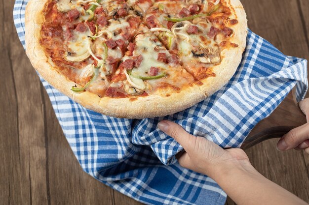 Holding a mix ingredient pizza on a blue checked towel.