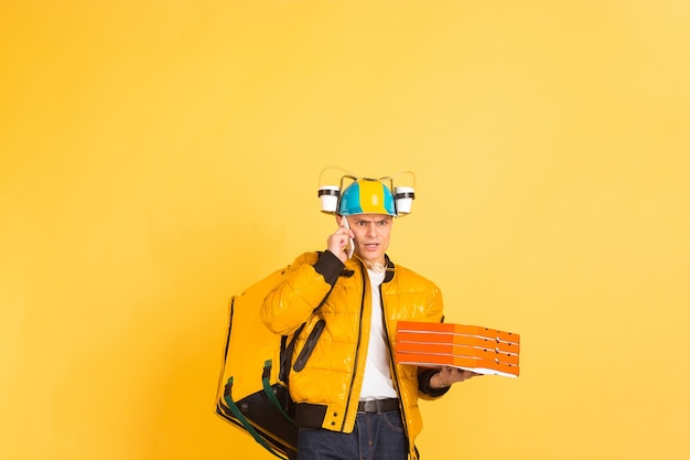 Free photo holding pizza, talking phone. emotions of caucasian deliveryman on yellow