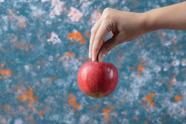 Holding a red apple from its stem