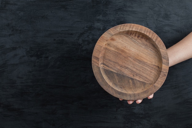 Free photo holding a round wooden board on black background