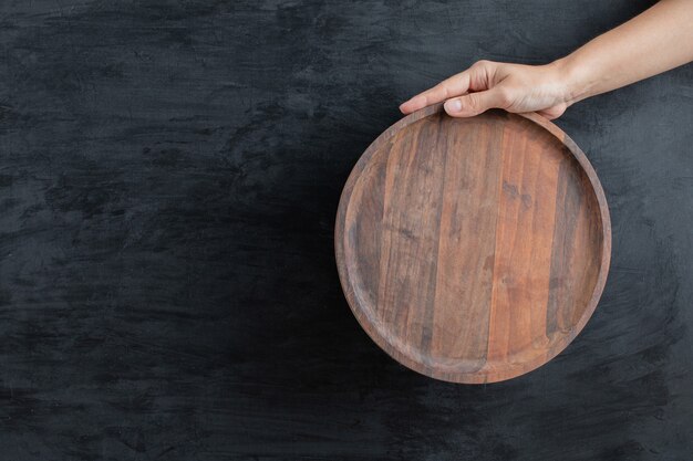 Holding a round wooden board on black background